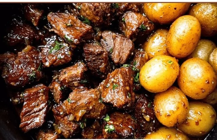 Delicious Garlic Butter Beef Bites served with crispy potatoes on a plate.