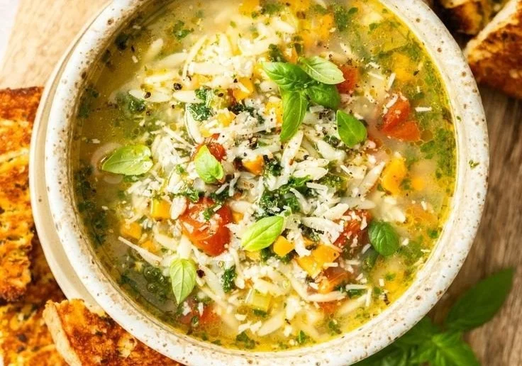 Bowl of Mediterranean orzo soup garnished with herbs and vegetables