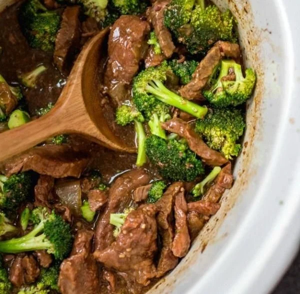 A bowl of slow cooker beef and broccoli served over rice, garnished with sesame seeds.