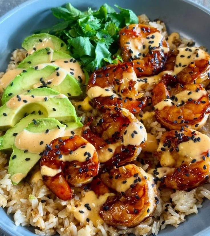 Teriyaki shrimp rice bowl with vegetables and sauce on a wooden table.